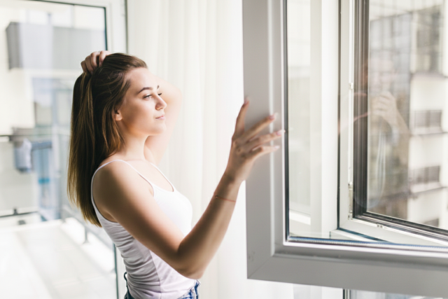 Mujer abriendo hacia el interior una ventana oscilobatiente de aluminio blanco con rotura de puente térmico.